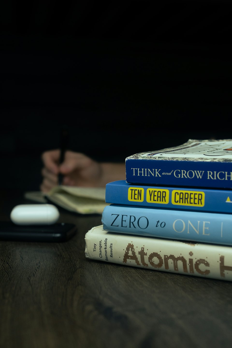 Books, smartphone, and earbuds rest on a wooden desk.