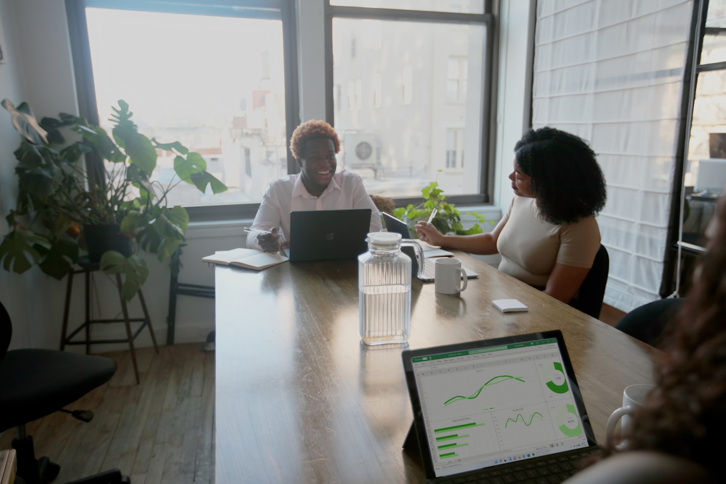 Two professionals discuss charts on a laptop at a conference table.