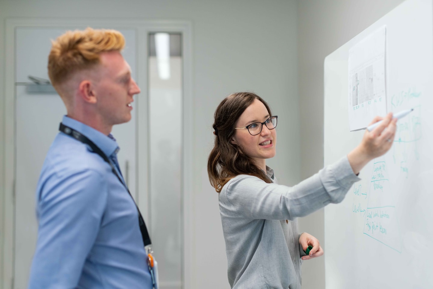 Two professionals collaborating on a whiteboard in a modern office.
